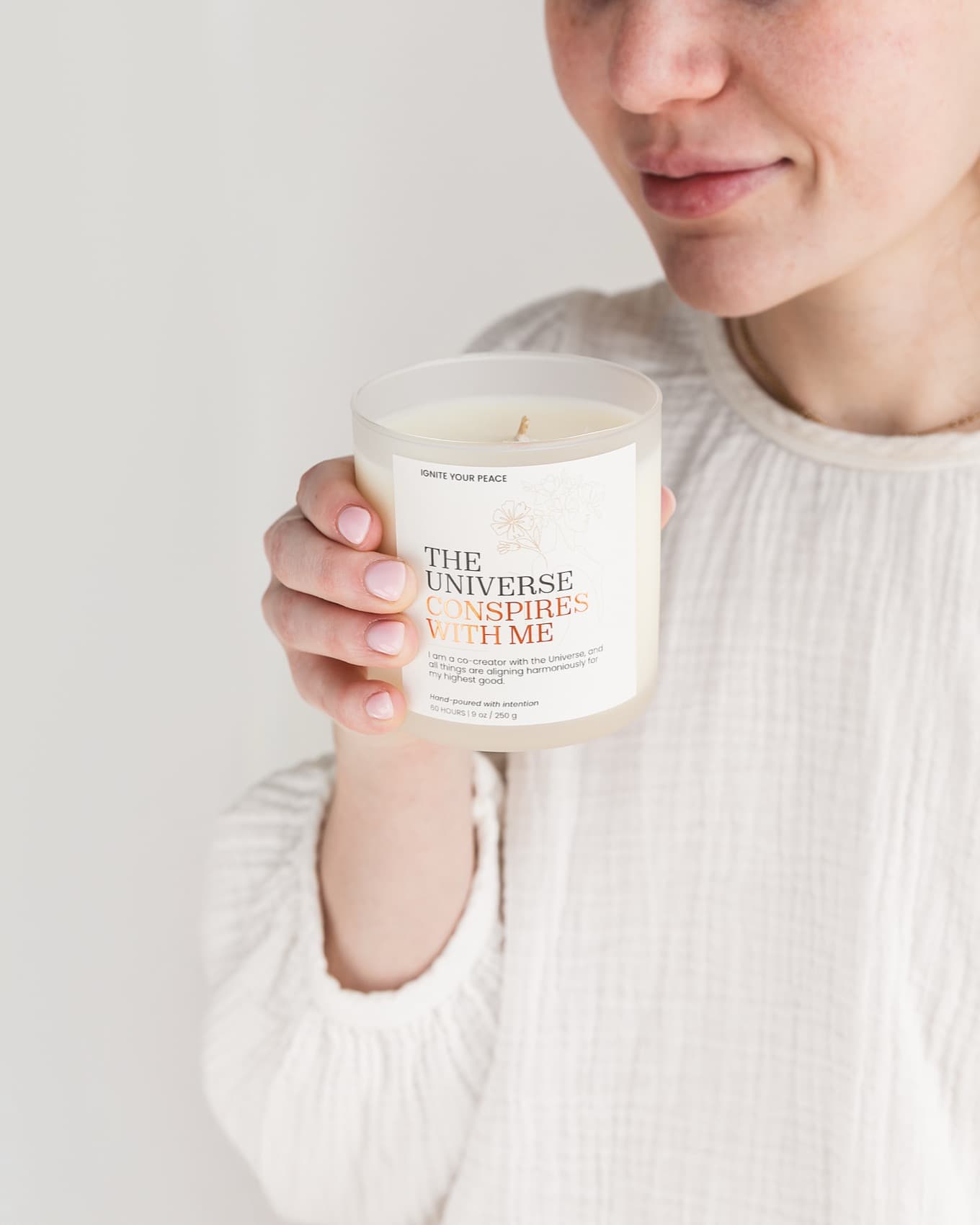 A woman holding an Ignite Your Peace affirmation candle in soft daylight