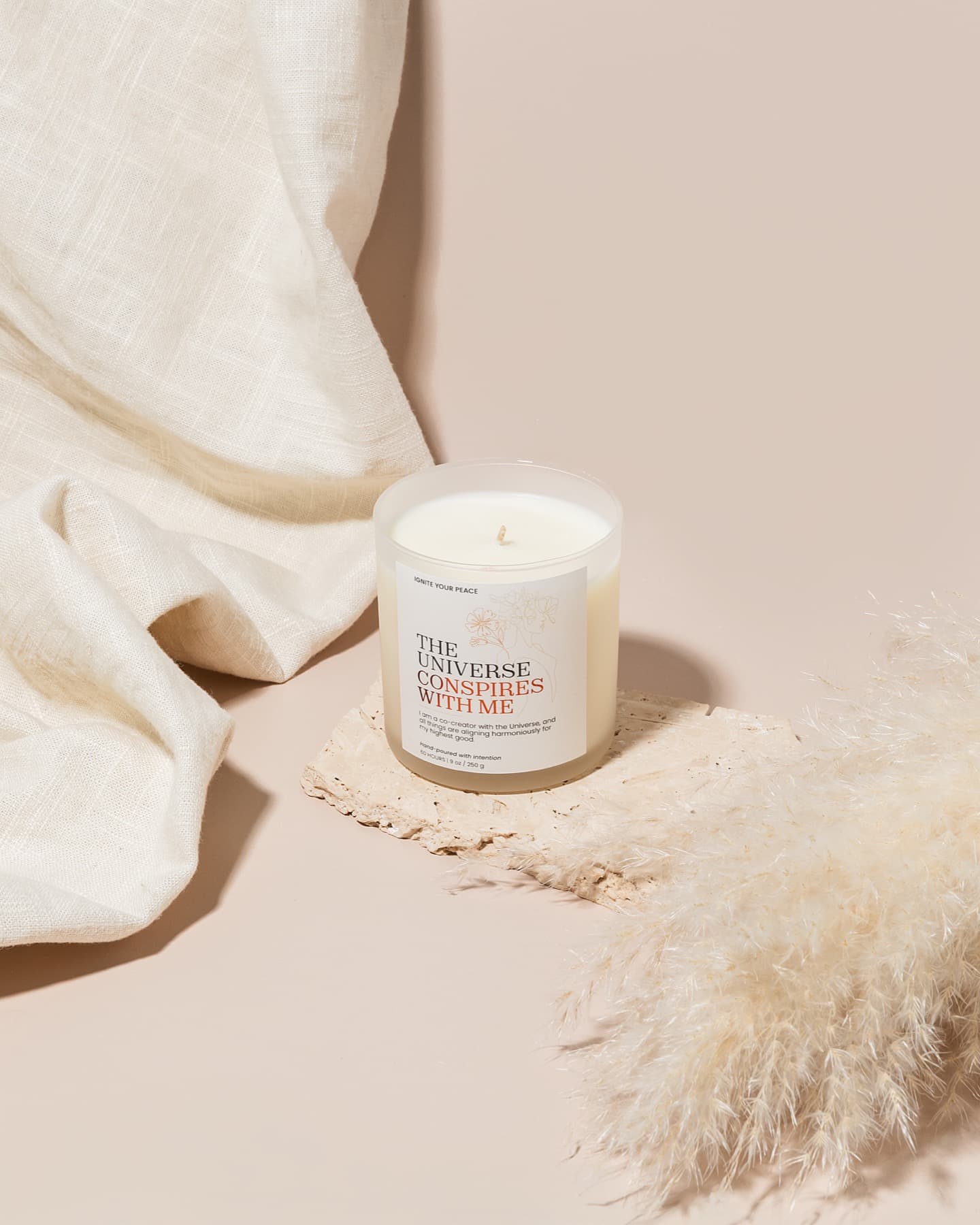 An Ignite Your Peace candle glowing beside linen and dried botanicals